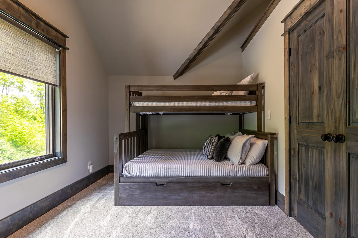 A playful bunk room featuring a bunk bed (twin over full), textured pillows, and a large window providing natural light. The space is designed to be both fun and restful, ideal for kids, cousins, or close companions.