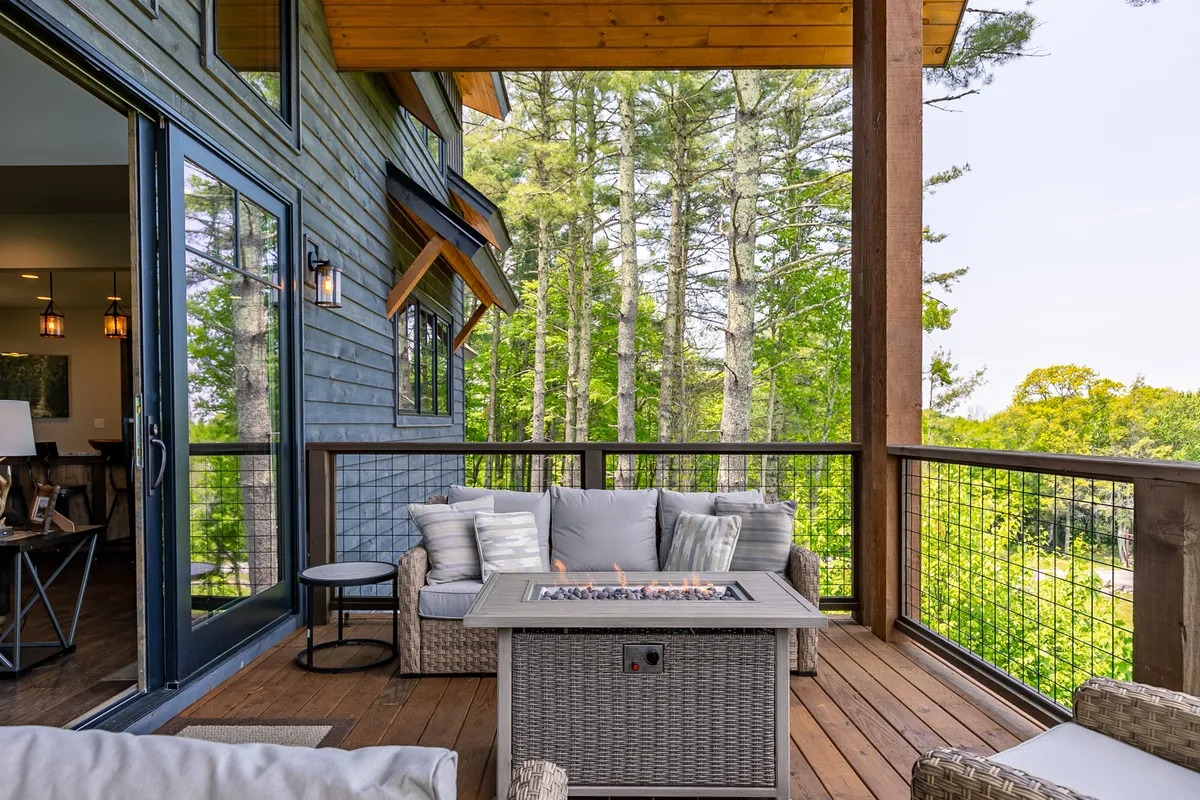 An inviting outdoor area featuring a fire pit encircled by comfortable seating. The scene is surrounded by trees, with a wooden railing framing the space, evoking a tranquil atmosphere perfect for evening gatherings, roasting marshmallows, or sharing stories under the stars.