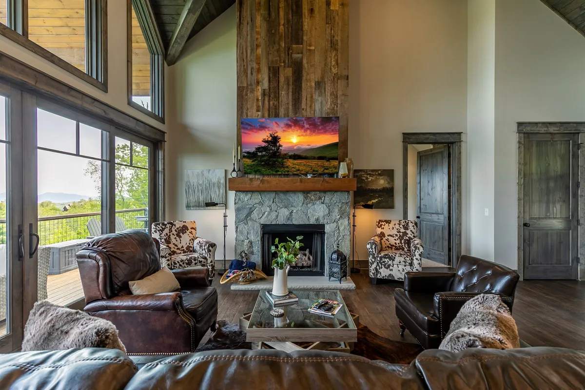 A welcoming living room centered around a large stone fireplace, with leather armchairs and expansive windows offering views of the surrounding landscape. The space feels open and connected to the outdoors, inviting guests (and their pets) to unwind after exploring.