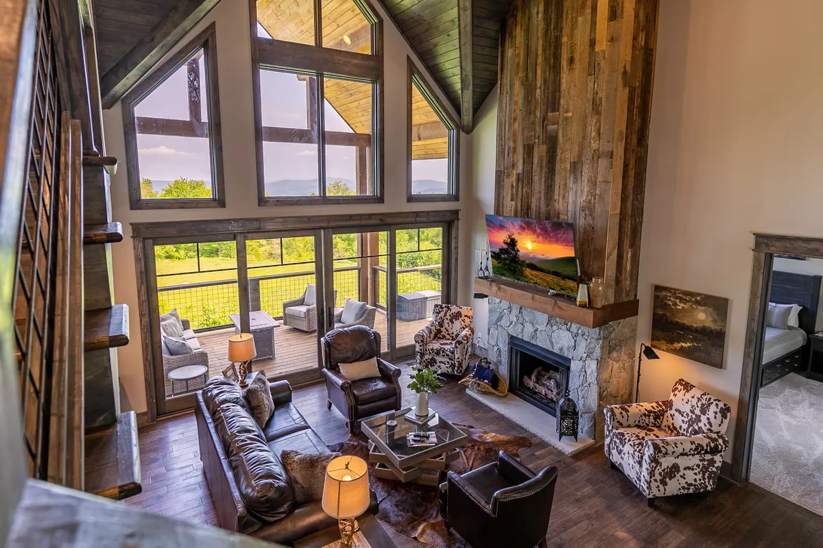 This inviting living area features large windows that frame stunning outdoor views, a cozy fireplace, and comfortable seating. The space seamlessly transitions to the deck, hinting at the cabin’s connection to the natural surroundings and easy access to outdoor activities.
