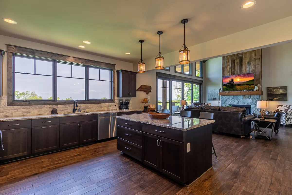 A modern kitchen scene with a large granite island, stylish pendant lighting, and expansive windows showcasing sunset views. The open layout is perfect for socializing, cooking, and entertaining guests.