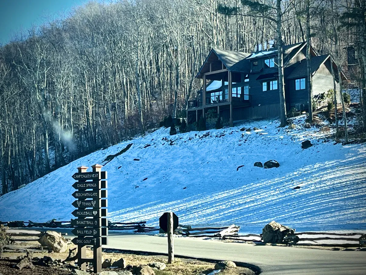 A picturesque mountain lodge stands amid a snowy landscape, with a signpost indicating various resort activities. The snow-covered ground and cozy architectural details evoke the winter adventure side of Eagles Nest, highlighting seasonal transformation and the lodge's central role.