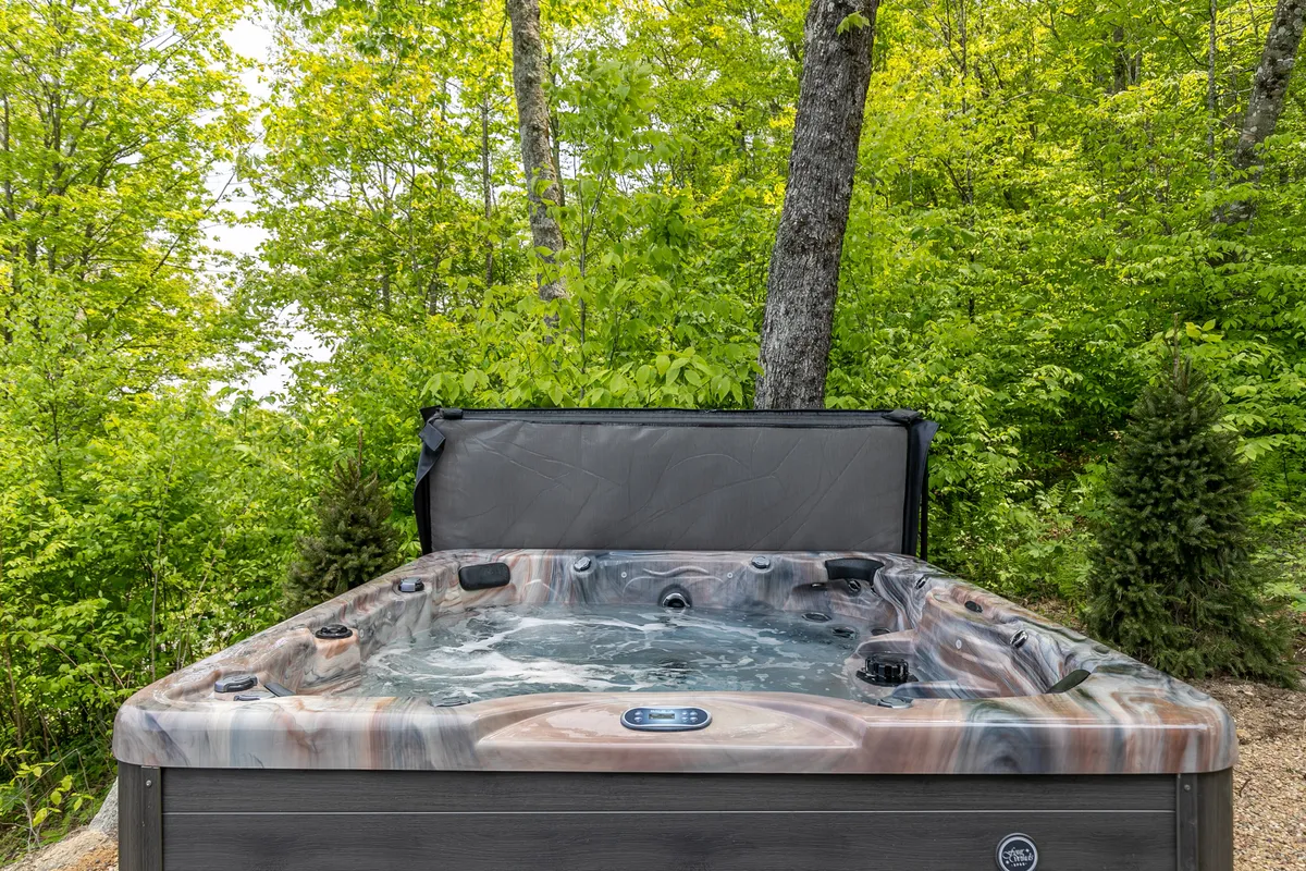 An inviting outdoor hot tub is nestled among lush greenery and tall trees. The tranquil setting offers privacy and direct immersion in nature, with ample space for couples or small groups to relax. The scene suggests both daytime relaxation and starlit evenings.
