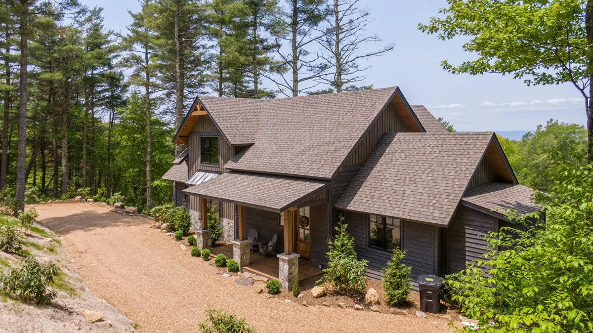A welcoming front porch adorned with sturdy stone columns and enveloped by towering trees. The inviting space suggests a peaceful spot to relax before or after a day of exploration, with easy access to nature trails and the outdoors.