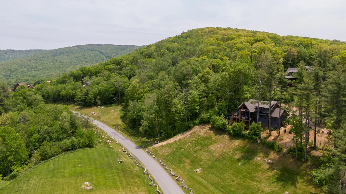 This exterior shot features a winding road leading up to a hillside house, surrounded by lush trees and natural landscape. The view hints at the outdoor adventure opportunities and scenic beauty accessible from the property.